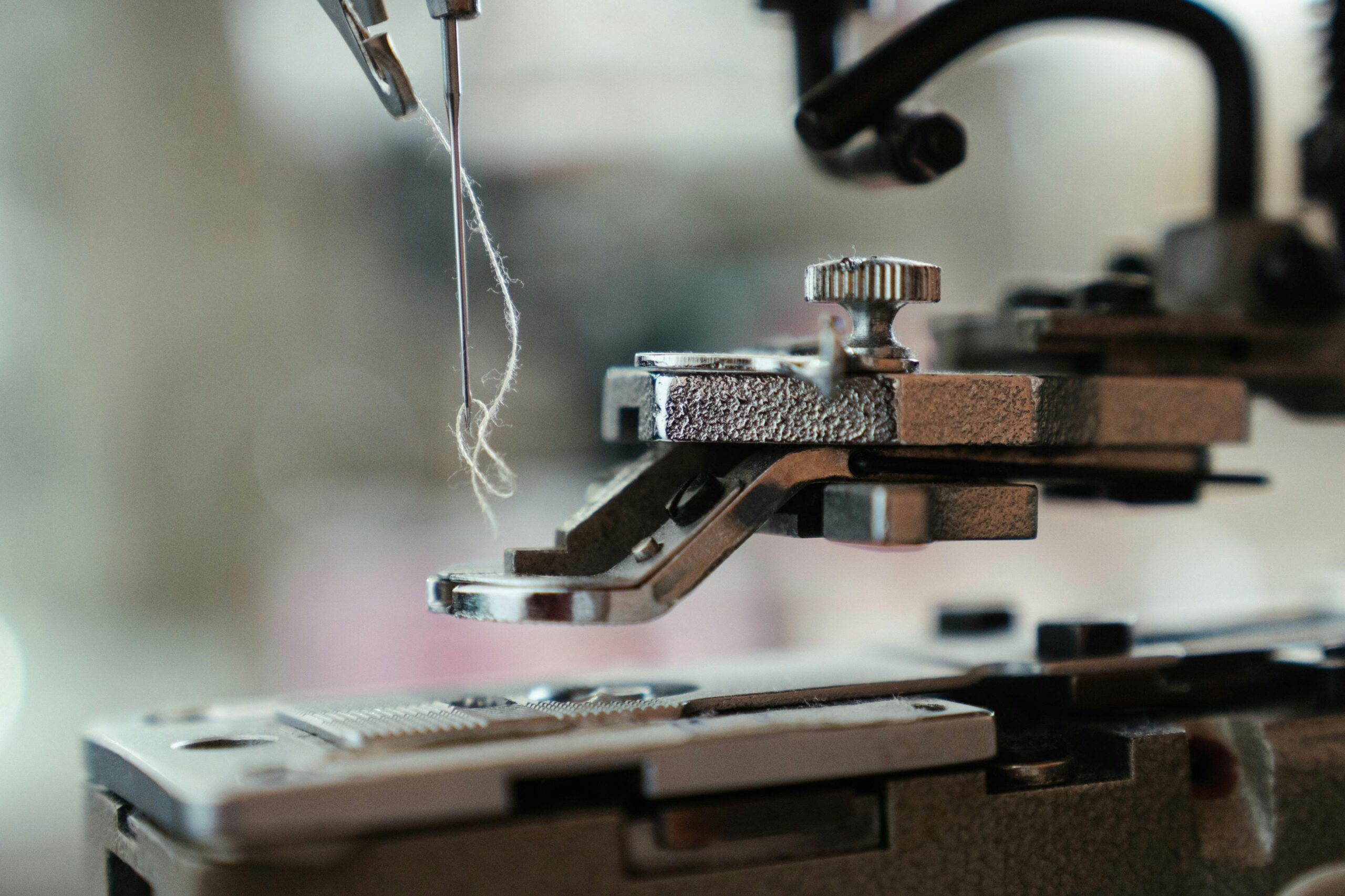 Detailed view of a sewing machine needle threading fine thread, showcasing precision in tailoring and craftsmanship.